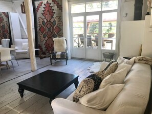 A spacious living area with a white sofa, a black coffee table, and a patterned armchair. A large window offers a view of the outdoors.