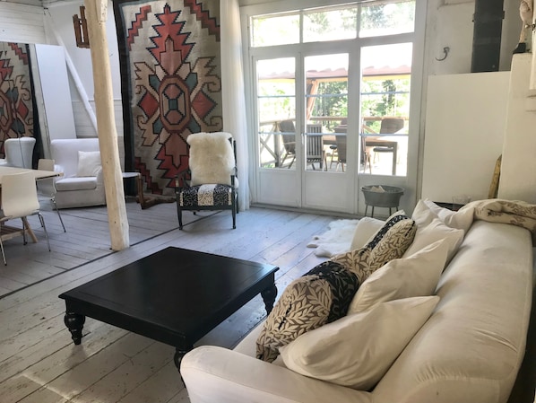 A spacious living area with a white sofa, a black coffee table, and a patterned armchair. A large window offers a view of the outdoors.