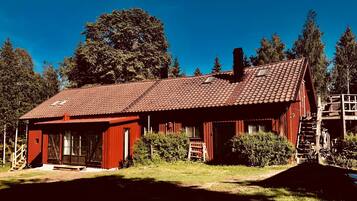 En röd trästuga med ett tak täckt av tegelpannor, en veranda och en trappa som leder upp till ett loft.