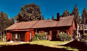 A red wooden cabin with a tiled roof, a front porch, and a staircase leading to a loft.