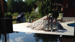 Un área de piscina con una vista despejada del cielo, una terraza de madera y una estructura de piedra.