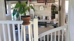 Una terraza de madera con barandilla blanca, una planta en maceta y un sofá blanco al fondo.