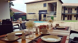 A dining area with tables set for breakfast, outdoor seating, and a view of the building in the background. - Palm Swift Luxury Accommodation (Brits)