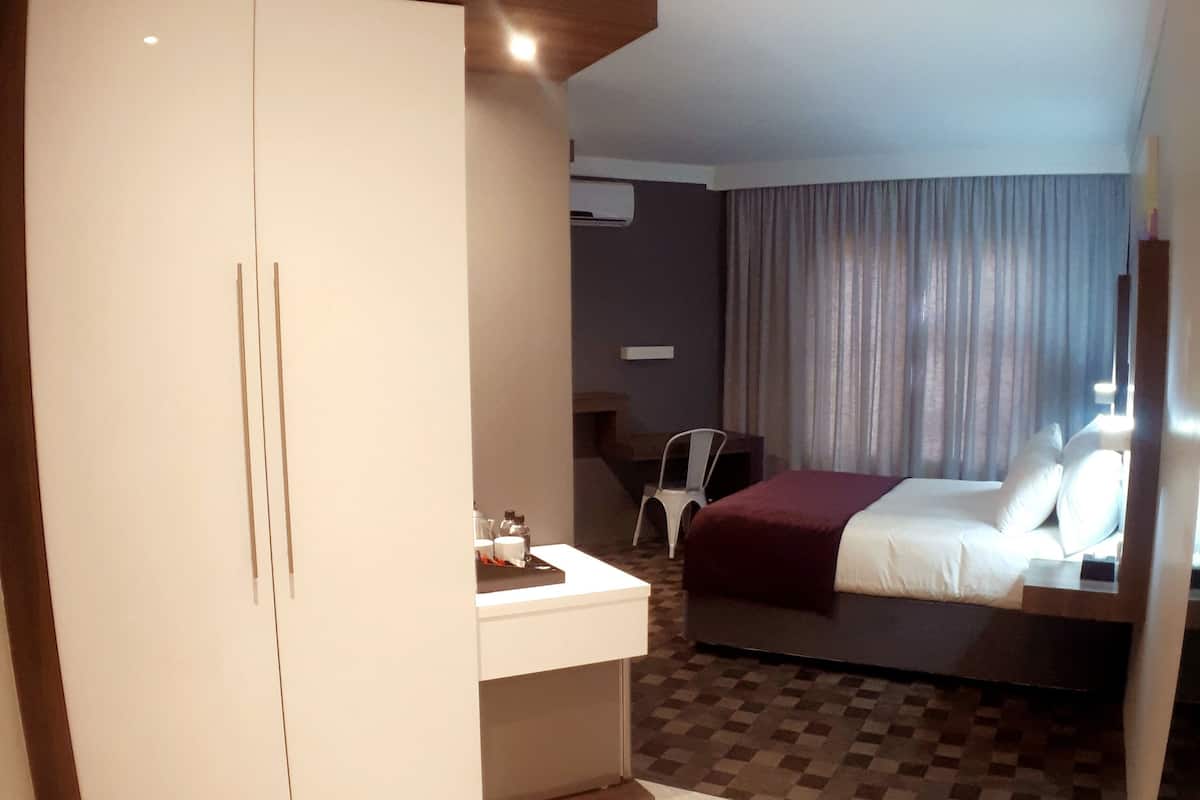 Quarto de hotel com uma cama, uma escrivaninha, um guarda-roupa e uma cadeira.