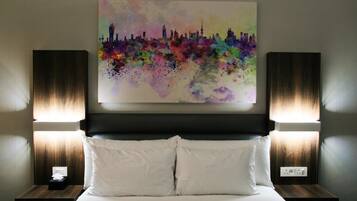 Quarto de hotel com uma cama, duas mesas de cabeceira, um quadro na parede e duas luminárias de parede.
