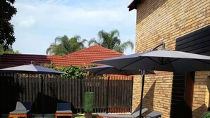 A swimming pool with lounge chairs and umbrellas, surrounded by a brick wall and a wooden fence. - Palm Swift Luxury Accommodation (Brits)