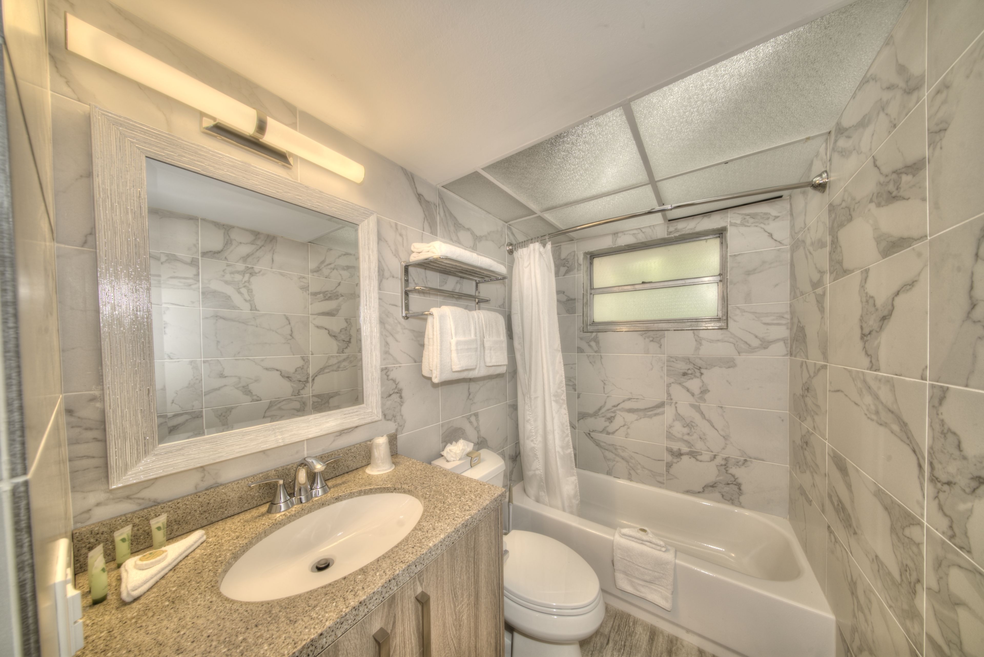 A bathroom with a marble-tiled wall, a sink with a granite countertop, a toilet, and a bathtub.