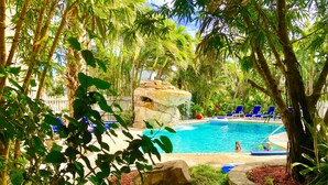 A pool area with a rock formation, surrounded by lush greenery and blue lounge chairs. - Riverside by the Beach Apartments (Pompano Beach)