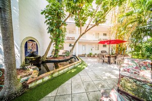 A courtyard with a fountain, seating area, and a red umbrella.