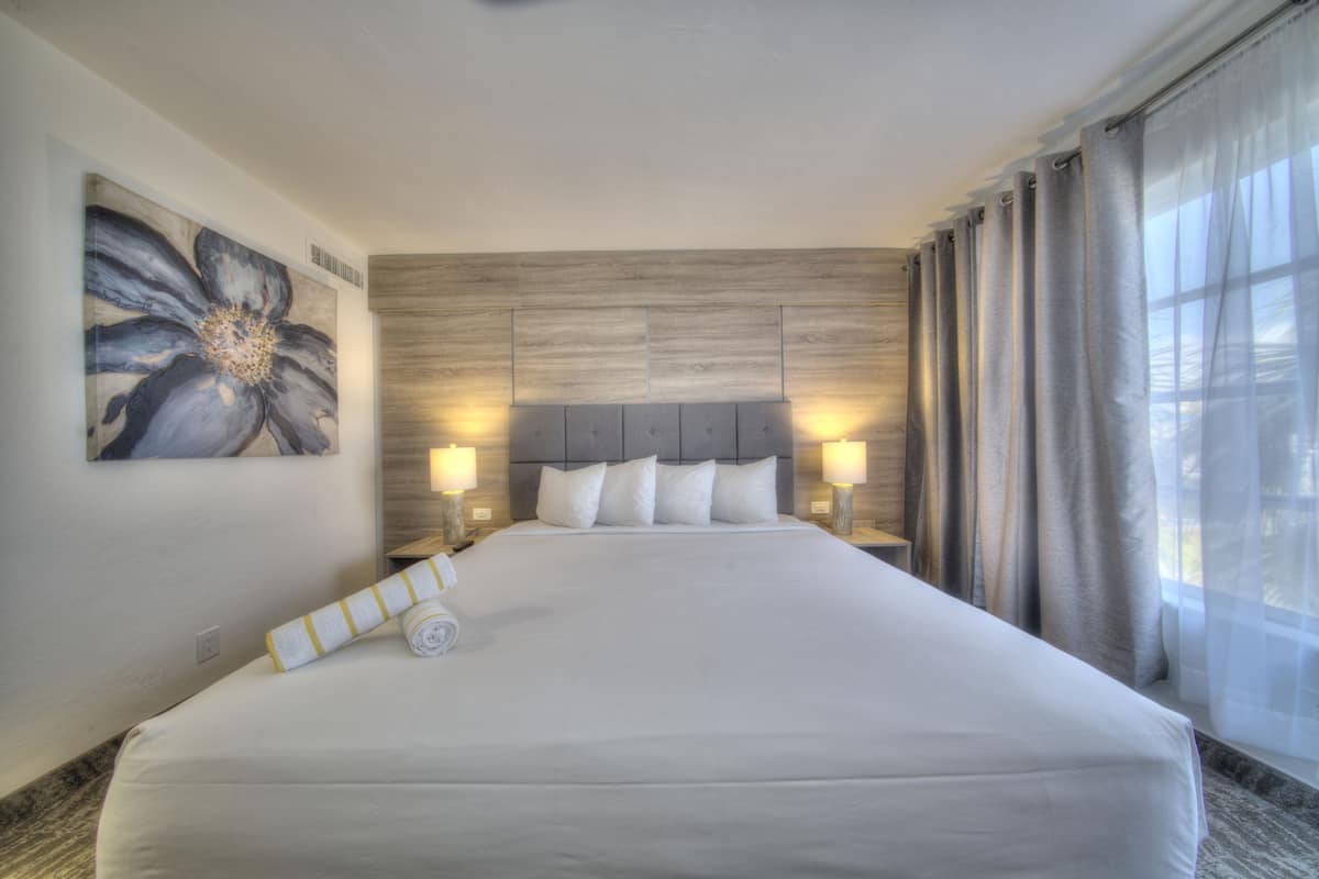 A large bed with a wooden headboard, two bedside lamps, and a large floral painting on the wall.