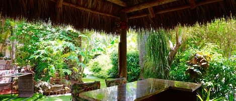 A thatched-roof structure with a bar area, surrounded by lush greenery and a well-maintained garden.