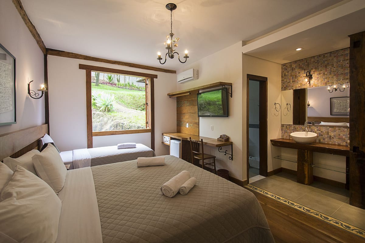 Une chambre avec un grand lit, un bureau, une télévision et une salle de bain équipée d’un lavabo et d’un miroir.