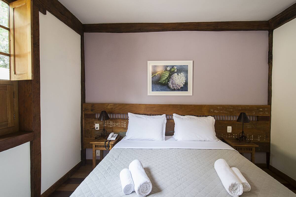 Un lit bien fait, avec deux serviettes enroulées, une tête de lit en bois, une table de chevet avec une lampe et un tableau encadré accroché au mur.