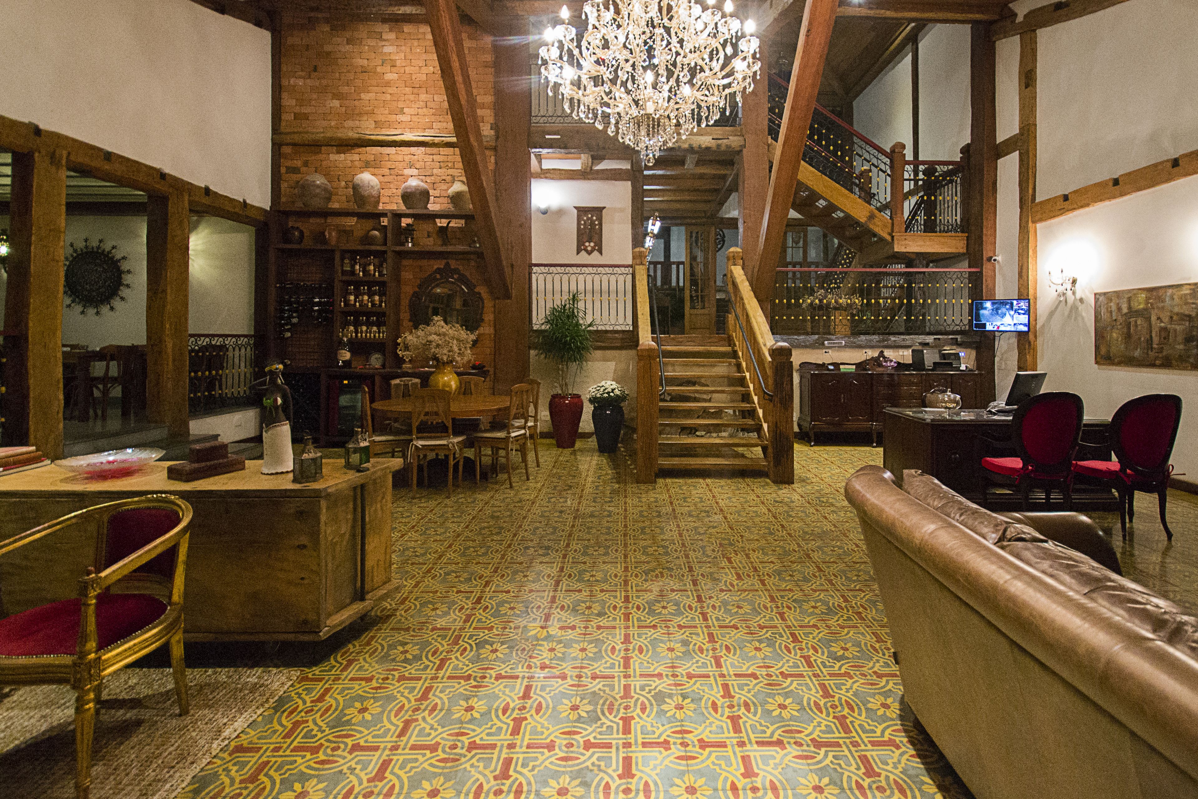 A spacious lobby with a patterned floor, a staircase, a bar area, and a seating area with a sofa and chairs.