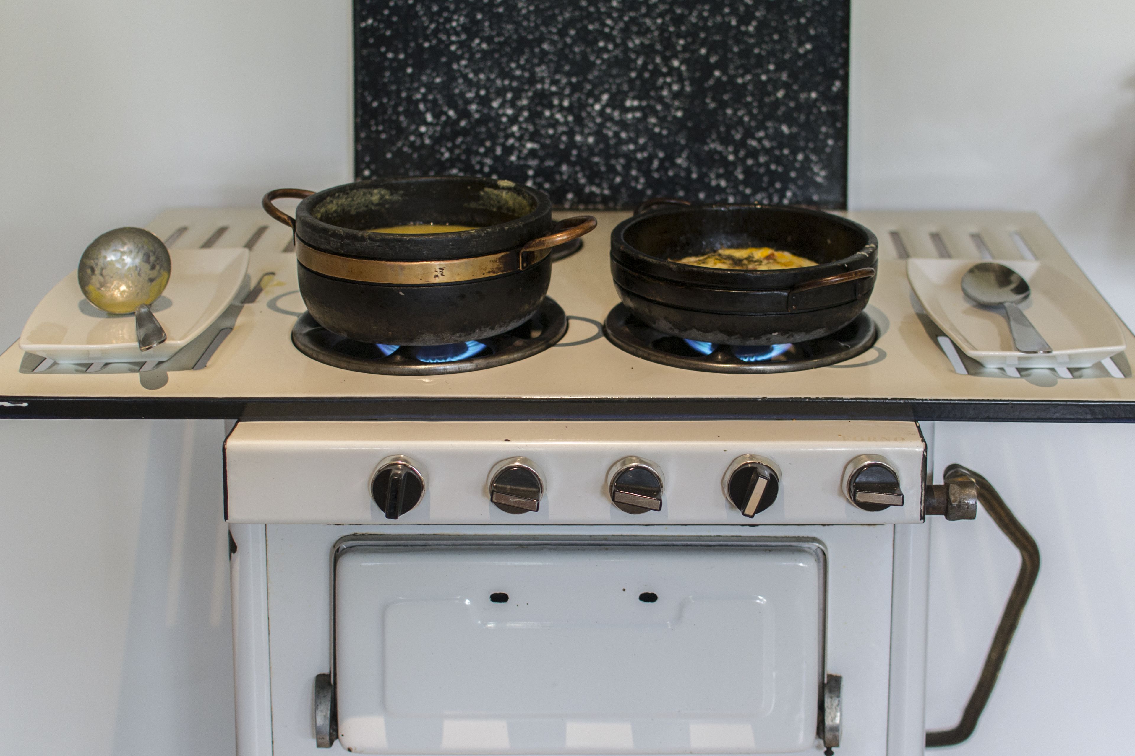 A kitchen with two black pots on a stove, a spoon, and a ladle on the counter.