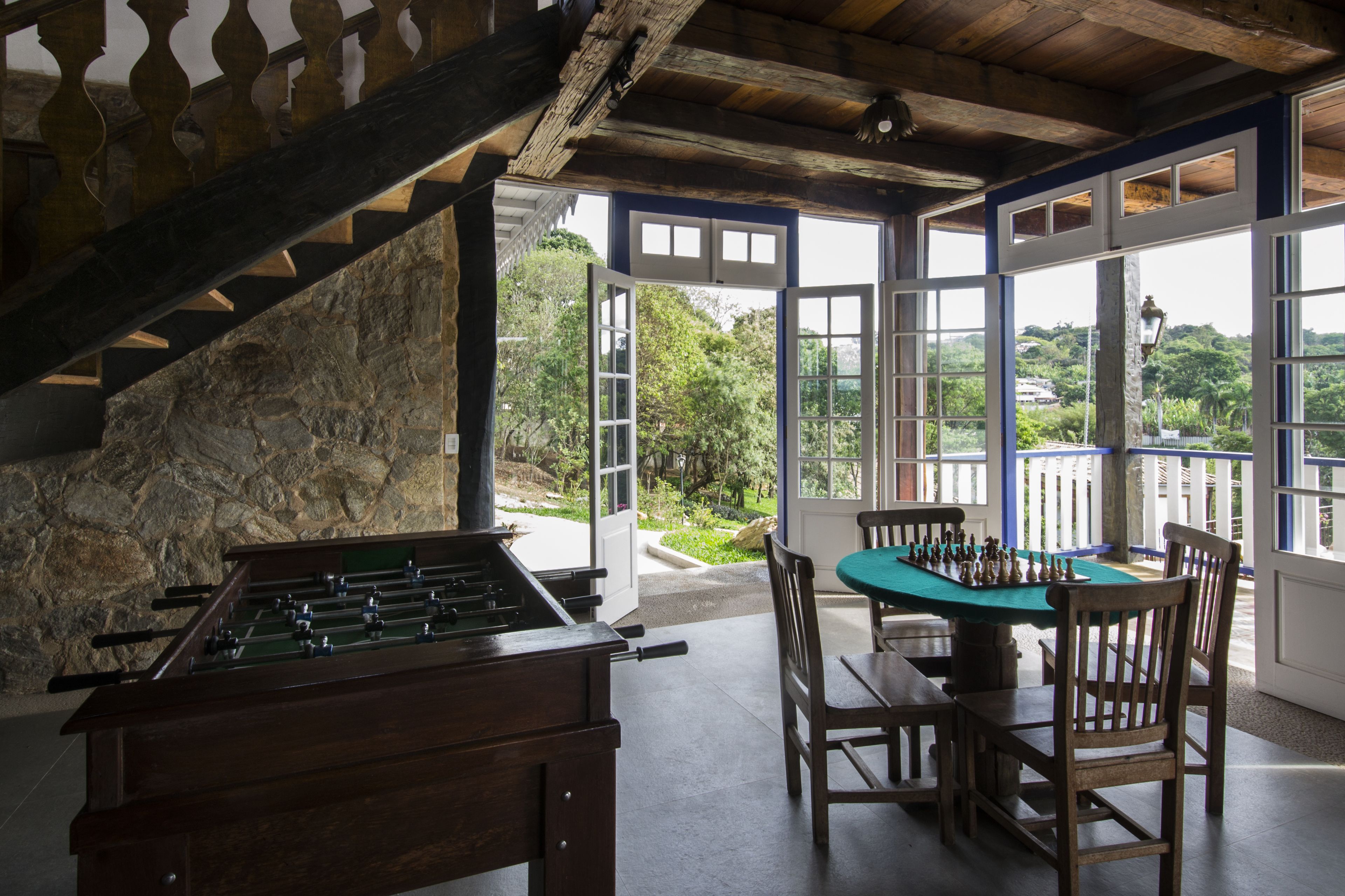 Quarto com mesa de futebol de mesa, um tabuleiro de xadrez e vista para o verde através de grandes janelas.