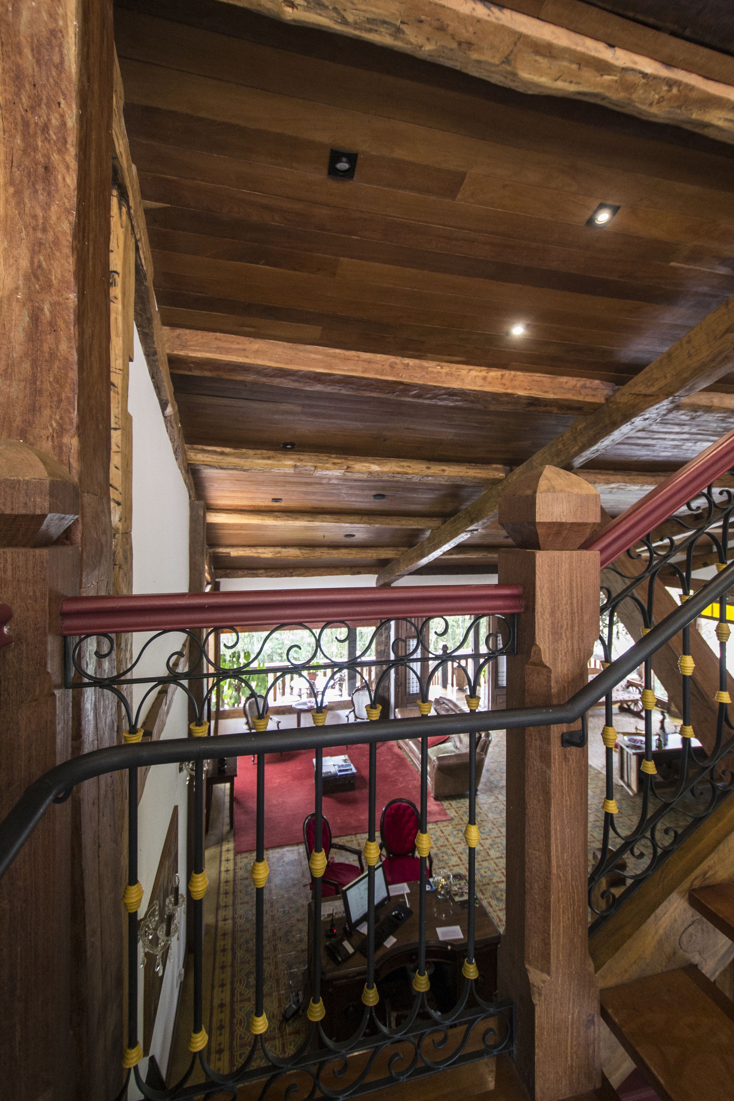 Una escalera de madera con barandilla de hierro forjado, que conduce a una habitación con una silla roja y una mesa.