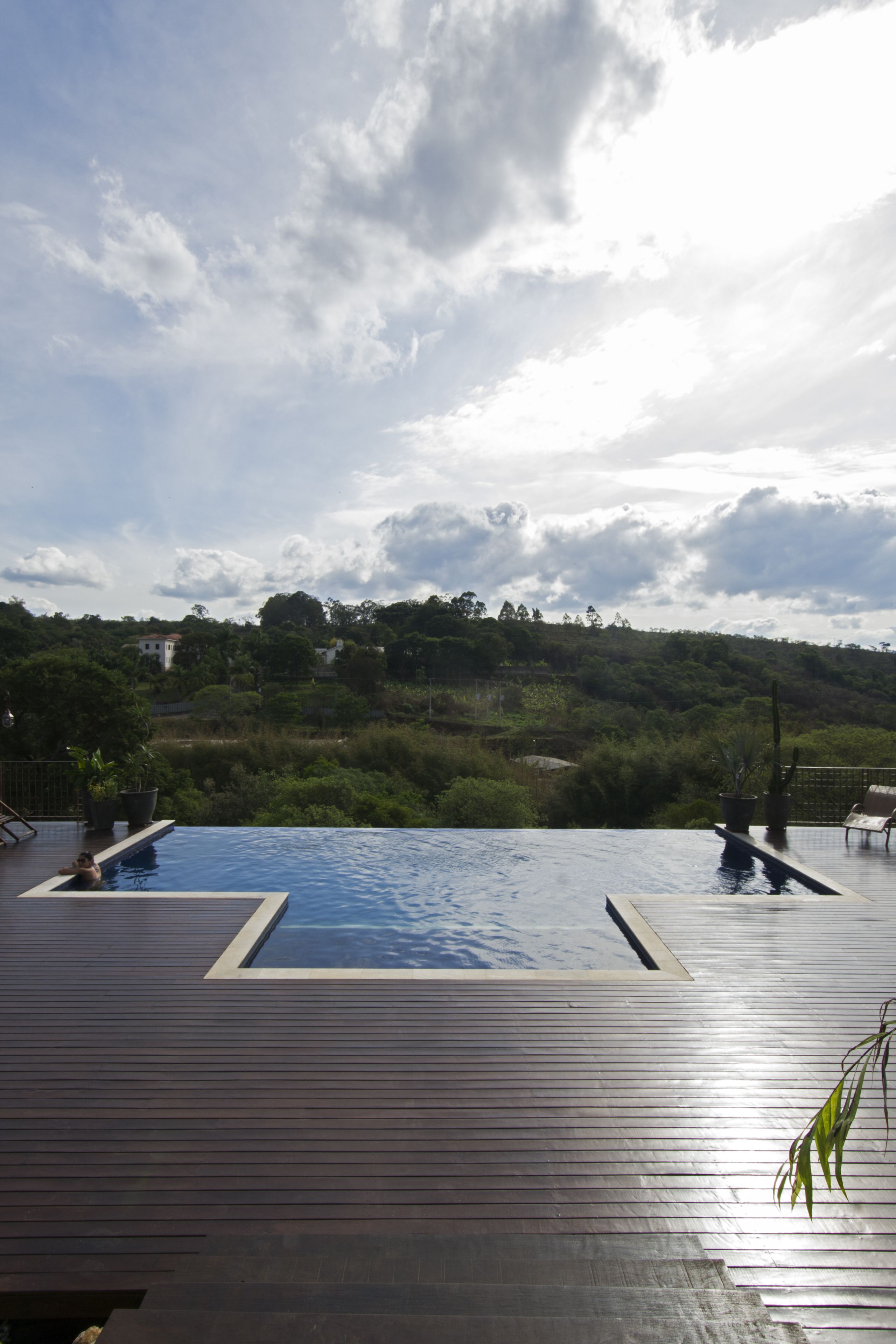 Una terraza de madera con piscina infinita y vistas a un paisaje verde y exuberante.