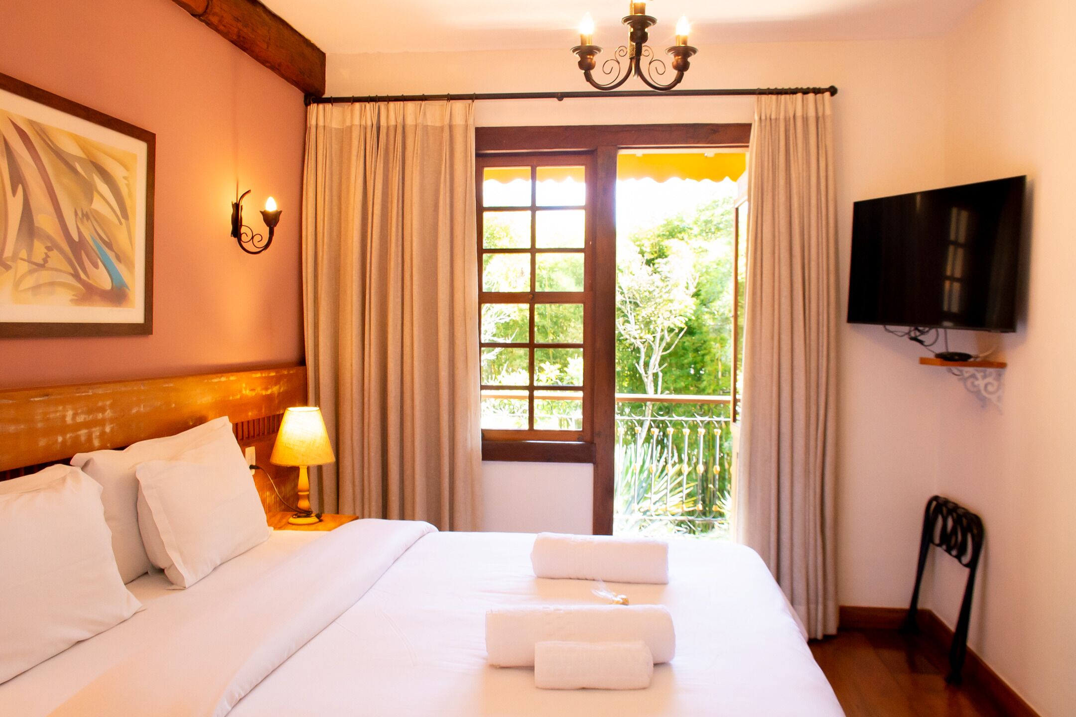 A hotel room with a bed, a TV, a window with curtains, and a painting on the wall.