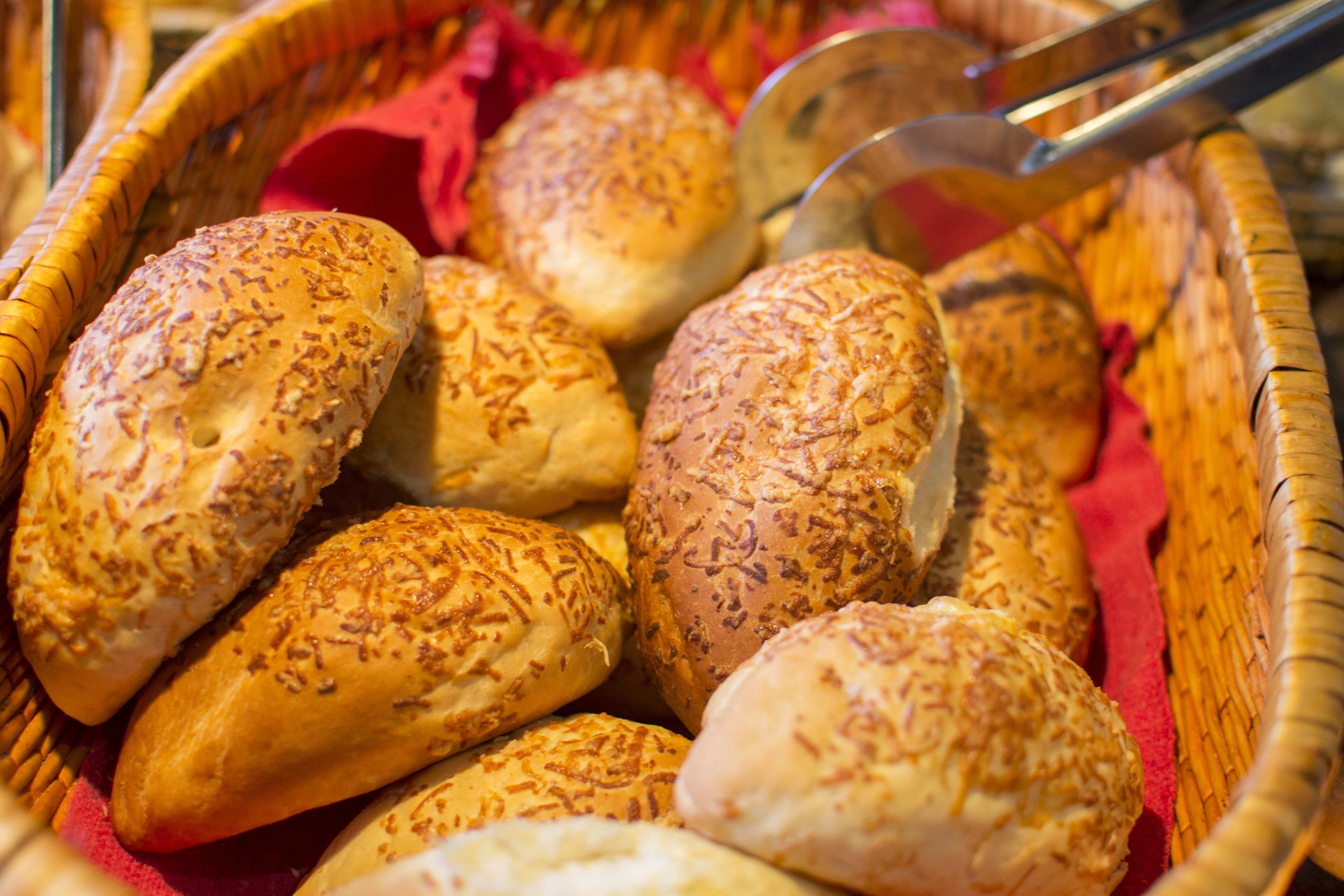 A basket filled with various types of bread, some with sesame seeds on top.