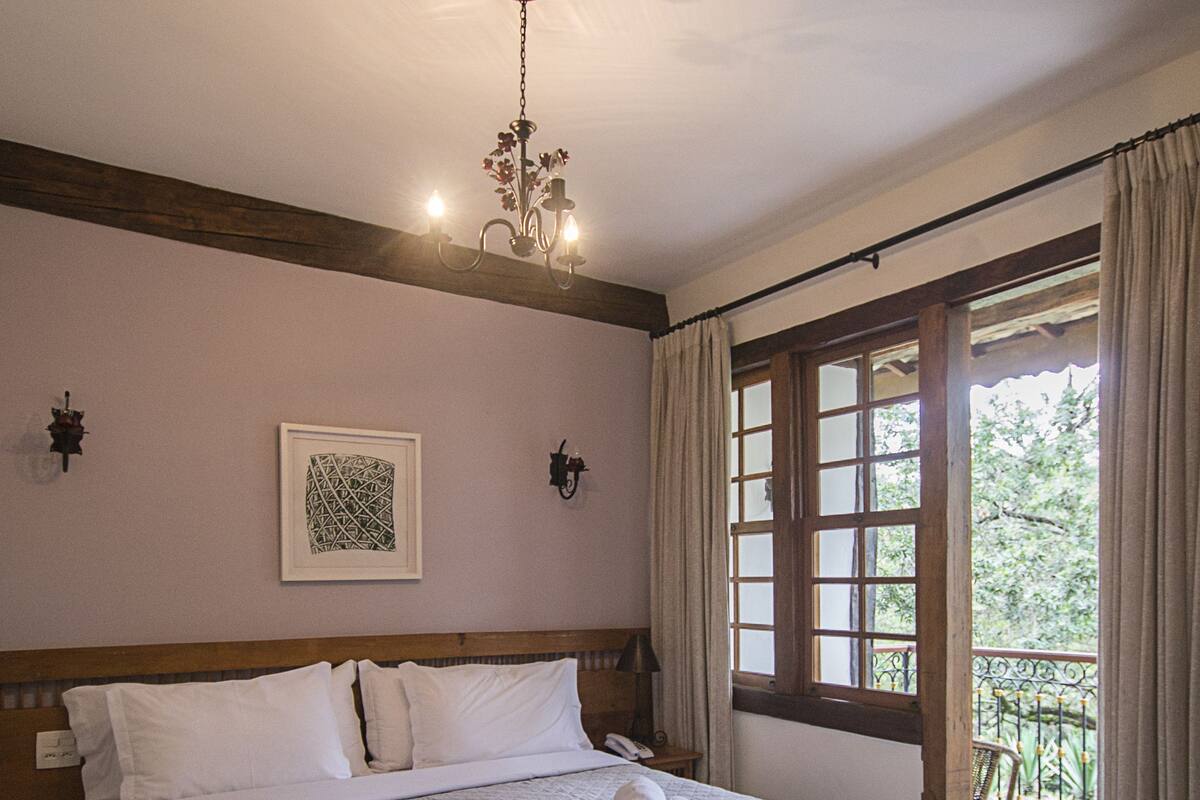 Un lit bien fait, recouvert d’une courtepointe matelassée, un lustre et une fenêtre avec des rideaux.