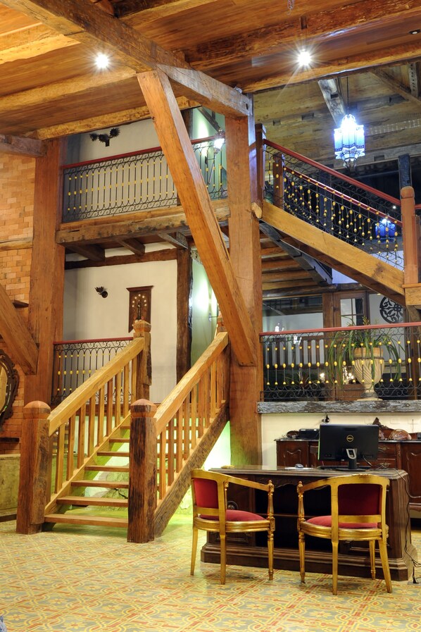 Una escalera de madera con barandilla, un escritorio con sillas y un piso con diseño.