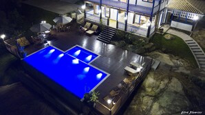 Una casa de dos pisos con piscina, mobiliario exterior y un patio bien iluminado.