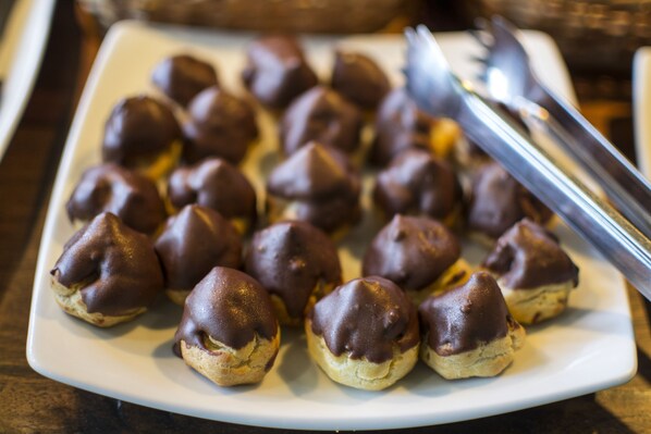A white plate with chocolate-covered pastries, a fork, and a knife on a wooden table.