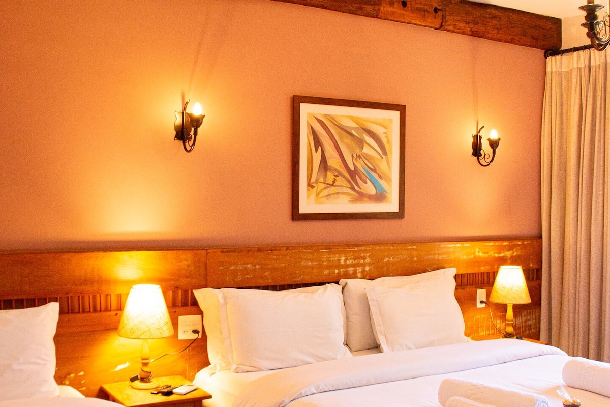 Une chambre d’hôtel avec deux lits, une tête de lit en bois, des lampes fixées au mur et un tableau.