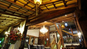 Un interior rústico con vigas de madera, una araña, una escalera y un jarrón de flores.