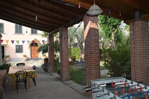 Ein Außenbereich mit einer Terrasse, einem Kicker, einem Tisch mit Stühlen und einer überdachten Sitzgelegenheit.