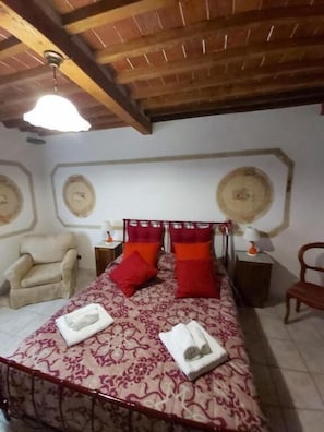 A bedroom with a bed, two chairs, a nightstand, and a ceiling fan.