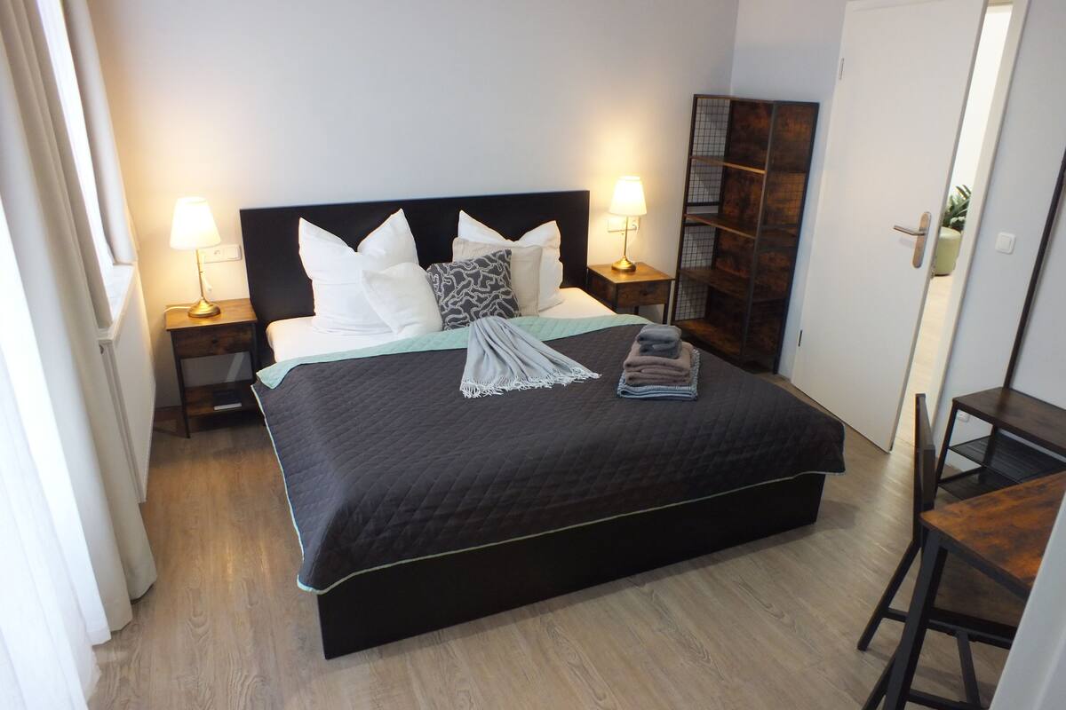Una camera da letto con un letto grande, due comodini con lampade, un armadio e un piccolo tavolo con sedie.