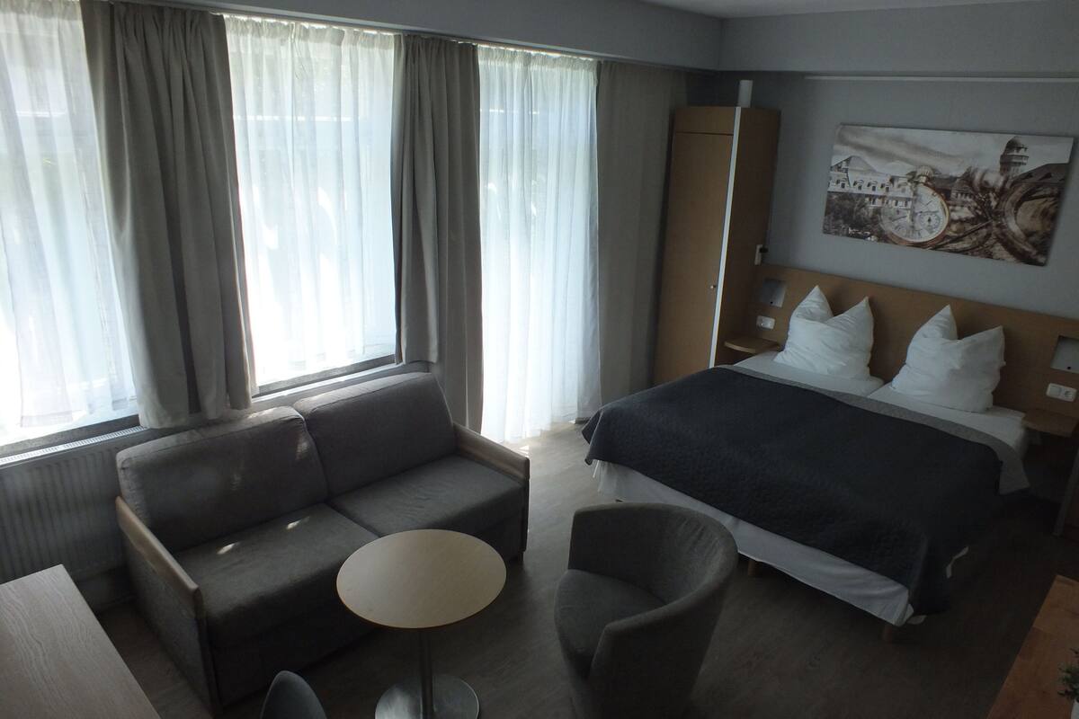 Una camera d'albergo con un letto, un divano, una poltrona, un tavolino e una finestra con tende.