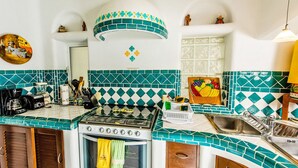 A kitchen with a stove, oven, and sink, featuring teal and white tiles and wooden cabinets. - Natz Ti Ha J101 by PRP (Playa del Carmen)