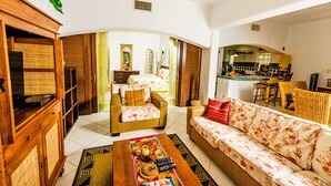 A spacious living room with a sofa, armchairs, and a coffee table. There is a dining area with chairs and a table. The room has a traditional design with wooden furniture and a tiled floor. - Natz Ti Ha J101 by PRP (Playa del Carmen)