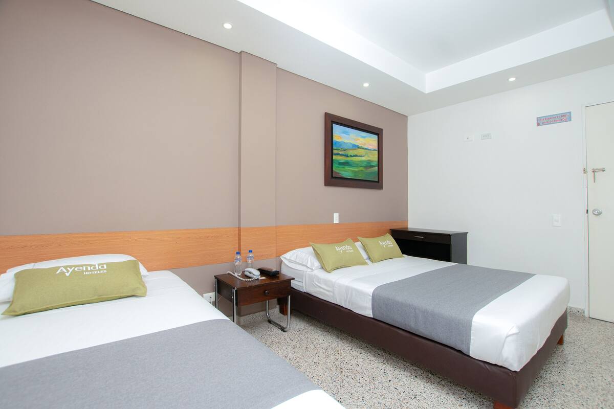 Een hotelkamer met twee bedden, een nachtkastje, een schilderij aan de muur en een deur met een bordje.