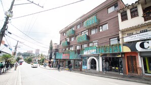 A street view with a building featuring multiple balconies, a pizza shop, and a store with a sign that reads "Optica." - Hotel  Oasis (Rionegro)