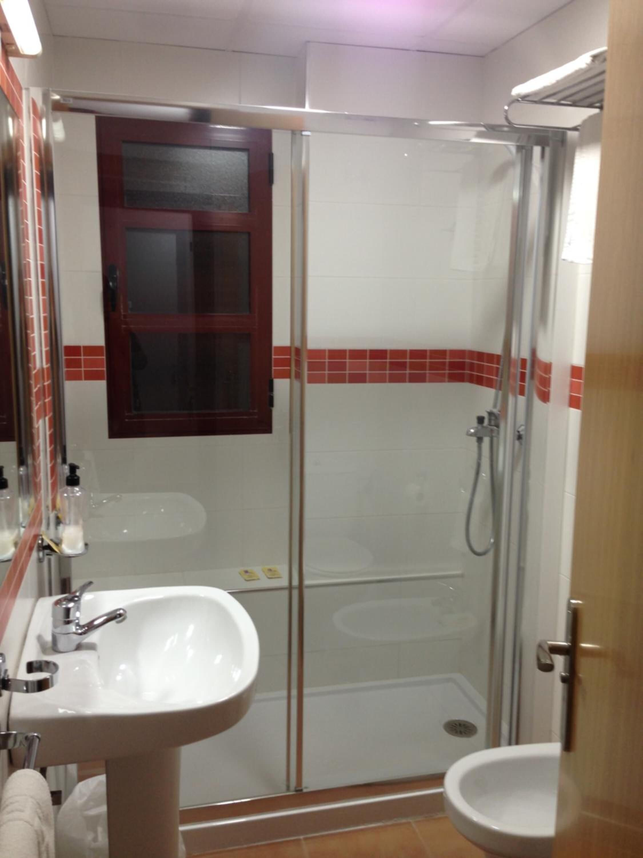 A bathroom with a glass-enclosed shower, a white sink, and a red-tiled shower area.