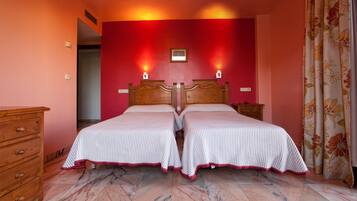A double bed with a wooden headboard, two bedside tables, a wooden dresser, and a red accent wall.