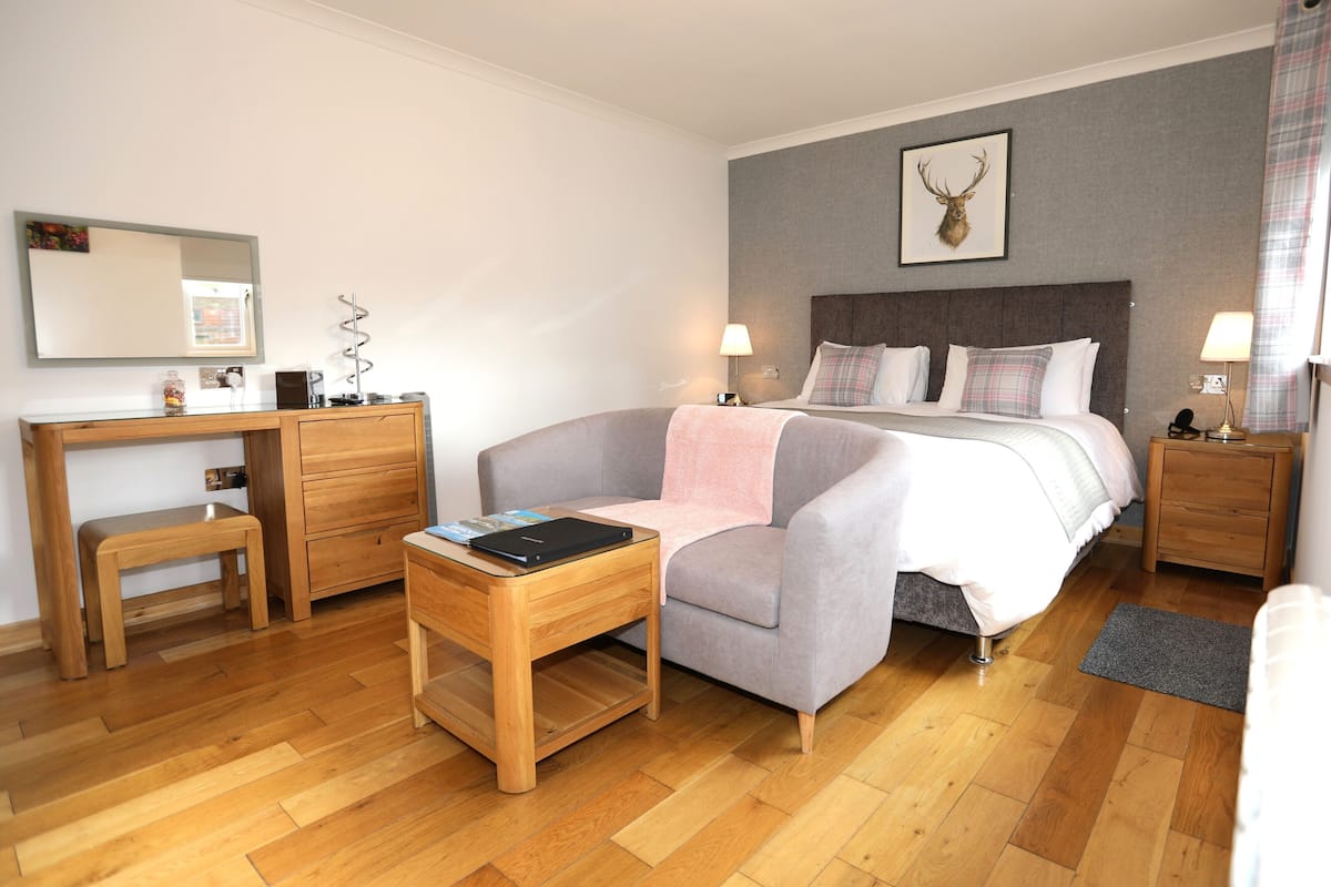 A bedroom with a bed, bedside tables, a desk, a chair, a mirror, and a wall-mounted picture.