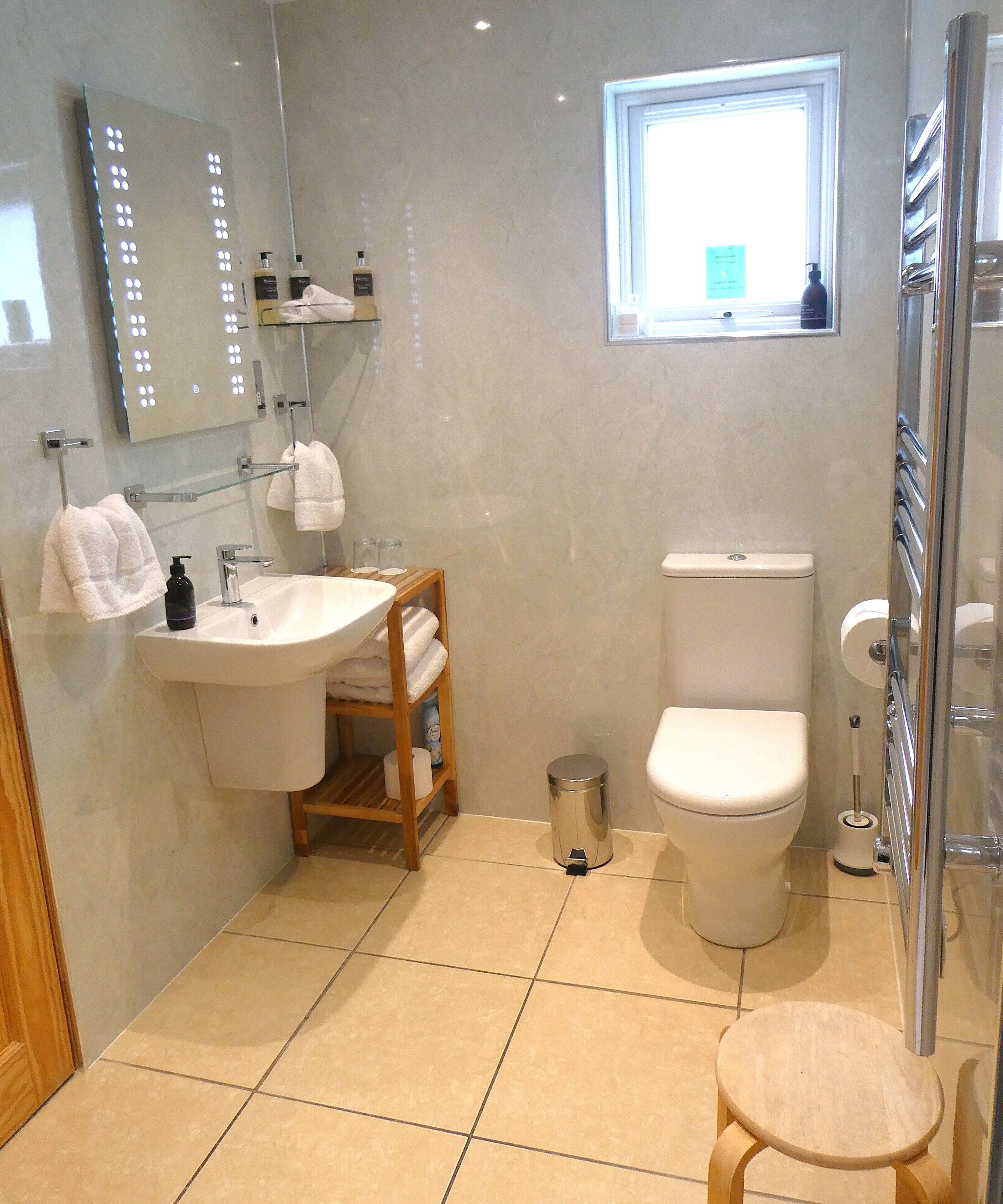 A bathroom with a sink, mirror, toilet, and a small stool.