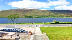Vista panorámica de un lago con un bote, un coche y una zona verde con una cerca y un banco.
