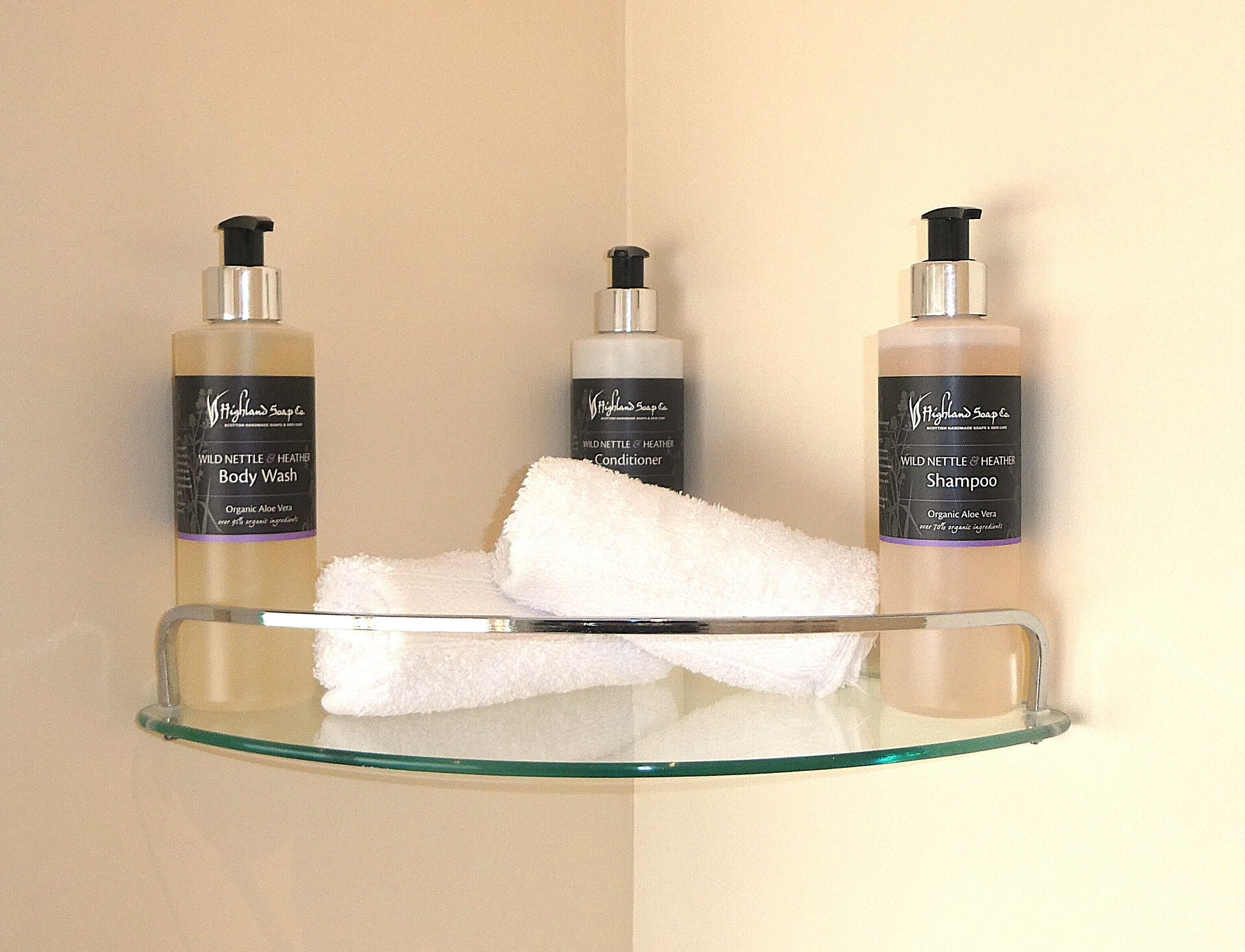 Three bottles of Wild Nettle & Heather body wash and shampoo on a glass shelf with a white towel.