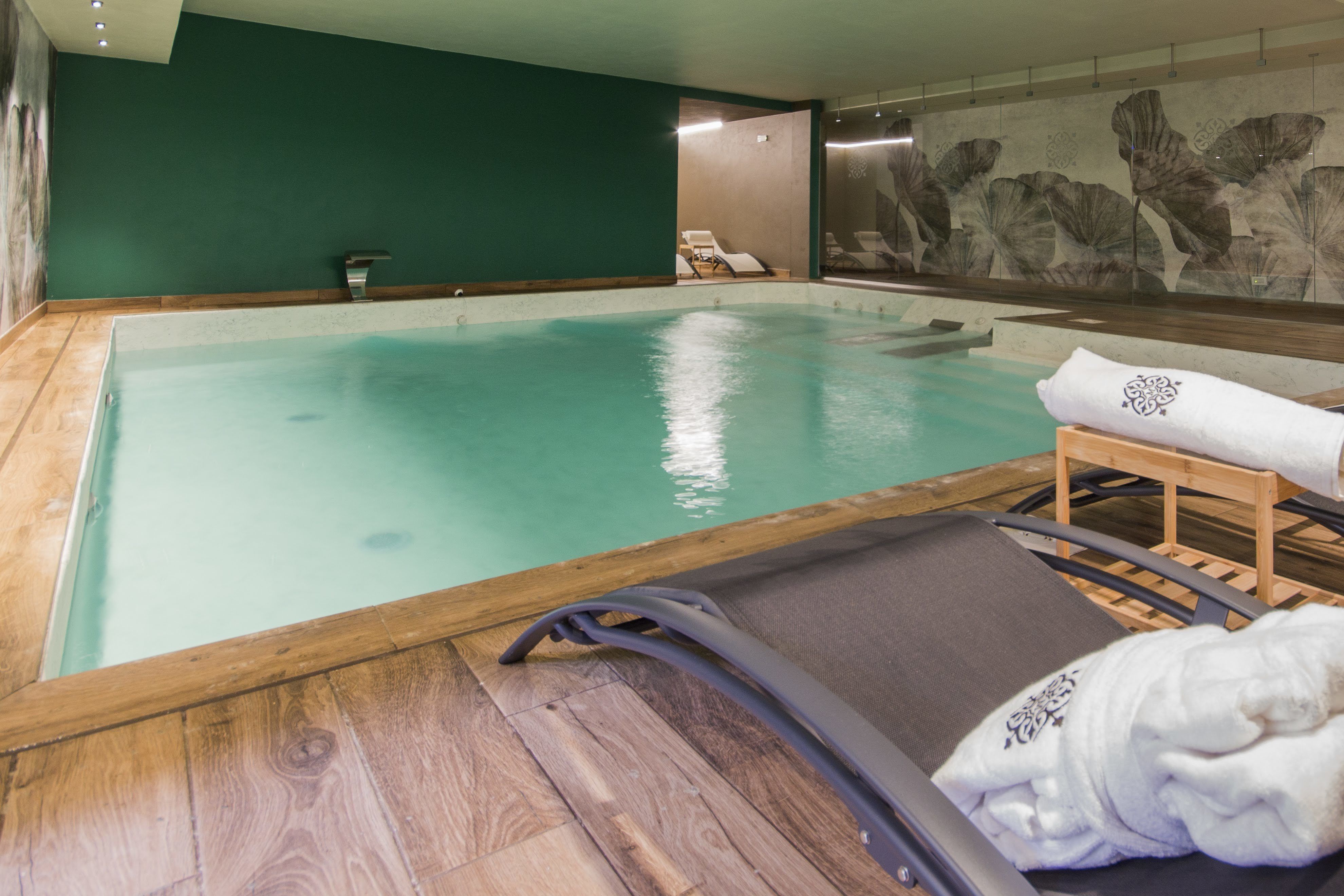 An indoor swimming pool with wooden flooring, a lounge chair, and a towel.