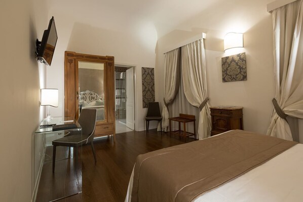 A hotel room with a bed, a desk with a chair, a TV mounted on the wall, and a wardrobe.