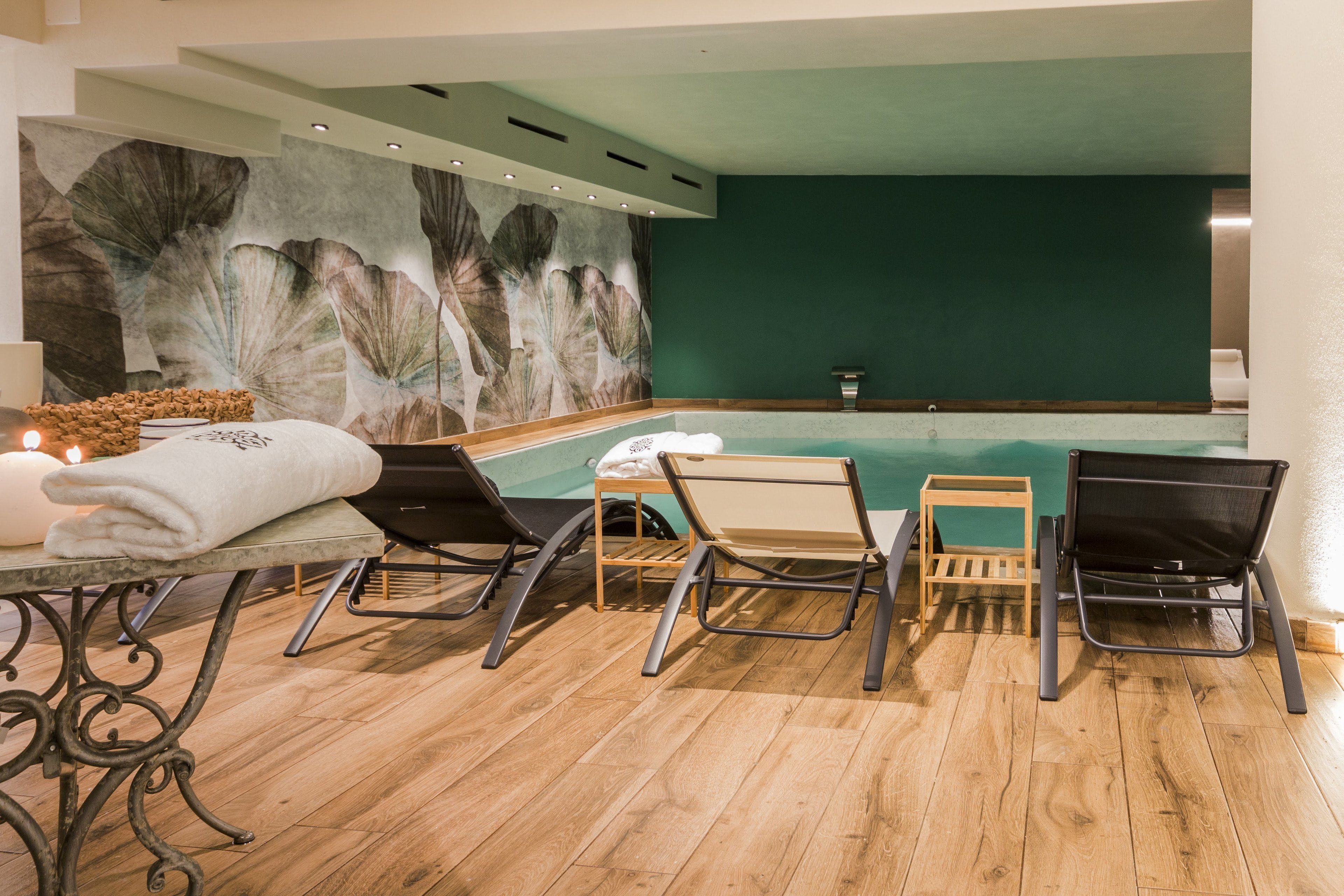 A spa area with a wooden floor, a large wall mural, a pool, and several lounge chairs.