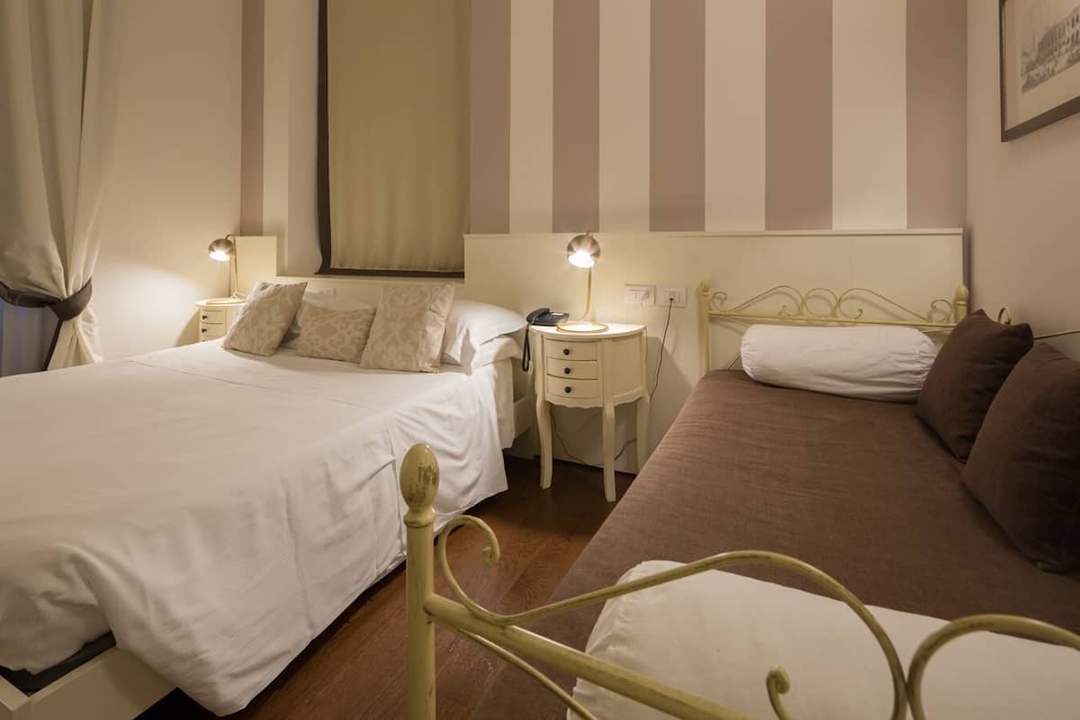 A hotel room with two beds, a bedside table with a lamp, a small desk, and a wall-mounted telephone.
