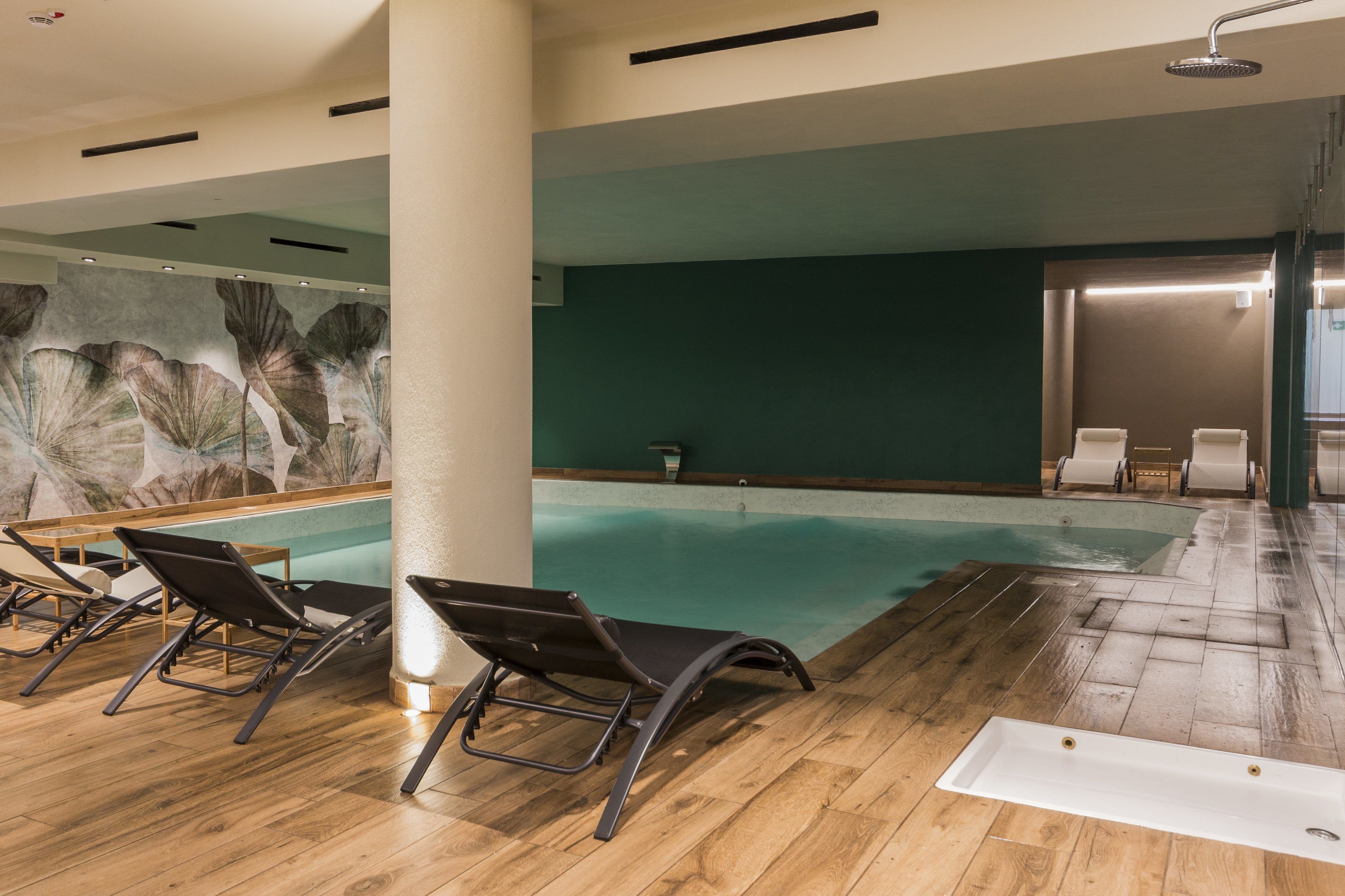 Una piscina interior con suelo de madera, sillones de descanso y un mural en la pared.