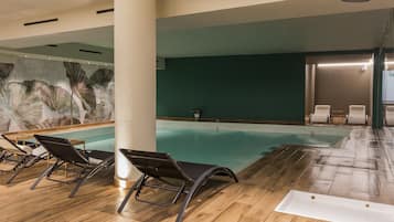 Una piscina interior con suelo de madera, sillones de descanso y un mural en la pared.